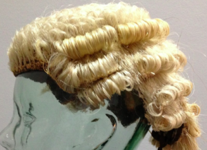 A blonde curled barrister's wig displayed on a glass head